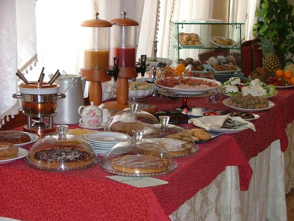 Ein reichhaltiges Buffet mit verschiedenen Speisen, darunter Gebäck, Früchte und Käse, unter Glaskuppeln.