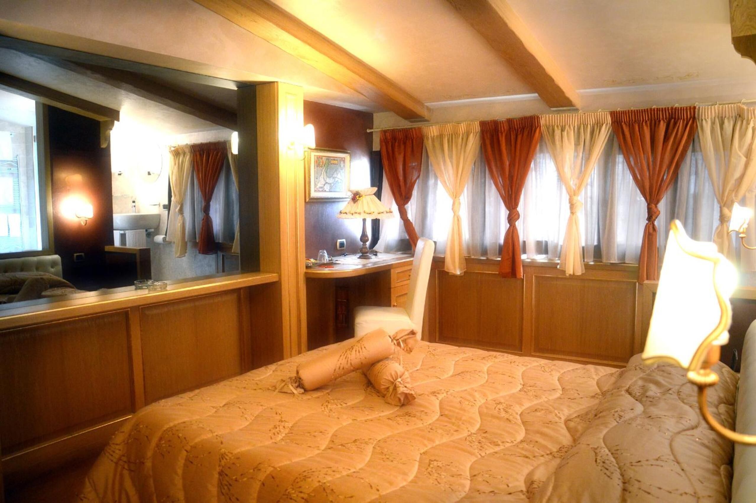 Habitació d'hotel amb un llit gran, una taula de treball amb una làmpada, un mirall i cortines.