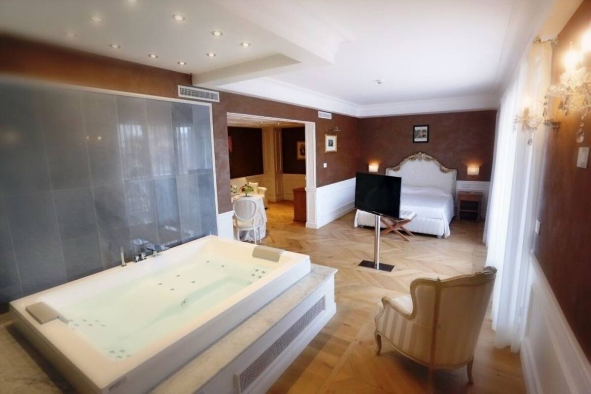 Un baño amplio con una bañera grande, zona de ducha independiente y un rincón acogedor con una silla y una mesita.