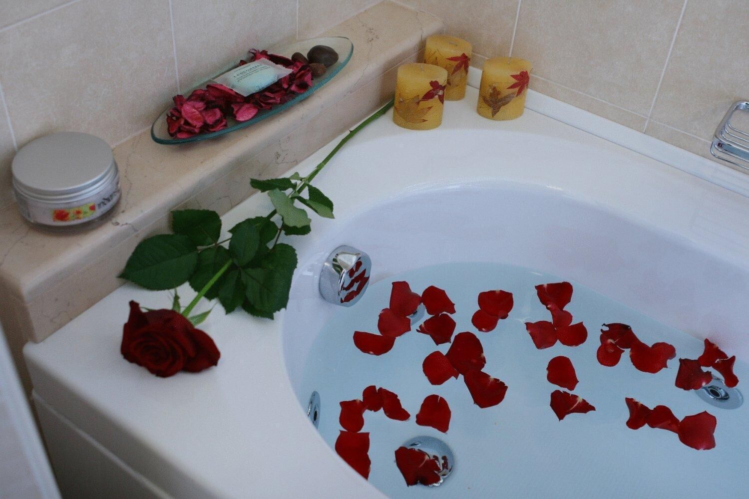 Une baignoire remplie de pétales de rose, une rose et des bougies.