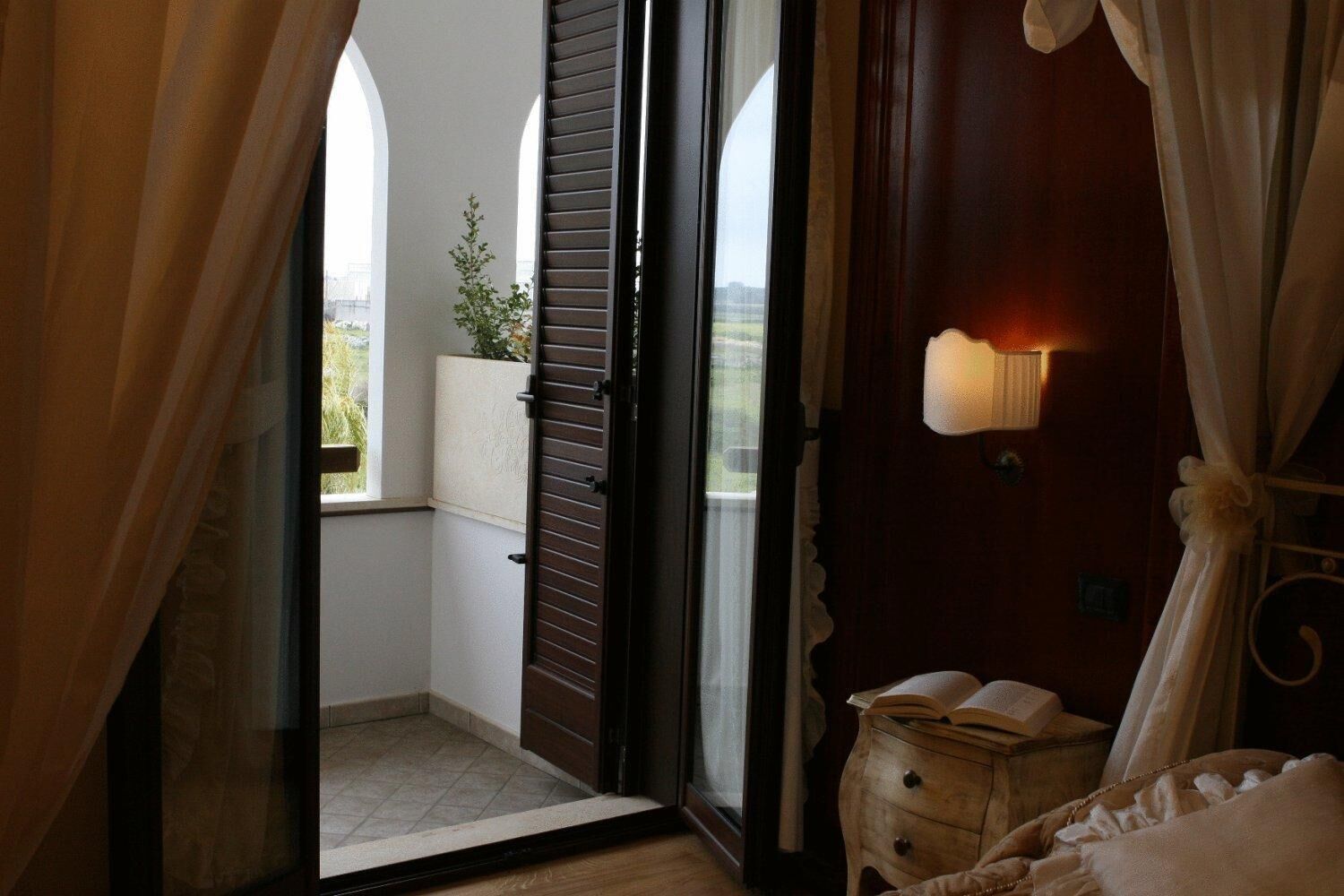 Un dormitorio con una puerta de vidrio corrediza que da a un balcón, una mesita de noche con lámpara y vistas al exterior.