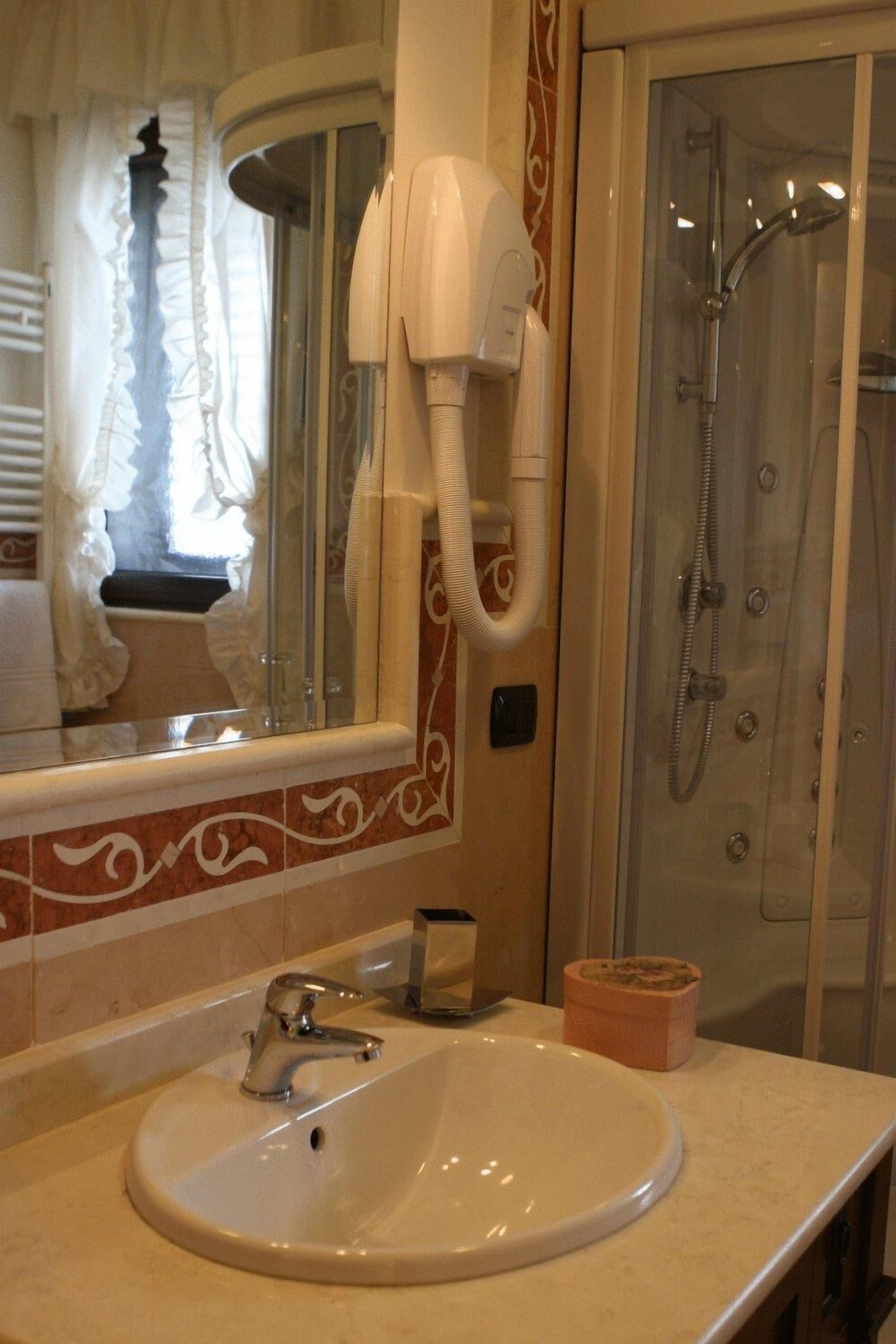 A bathroom with a sink, a mirror, a shower, and a hairdryer.