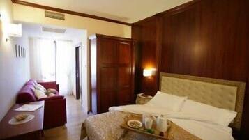 Una camera d'albergo con un letto grande, un comodino con un vassoio per la colazione, un'armadio in legno e una zona salotto con divano e tavolino.