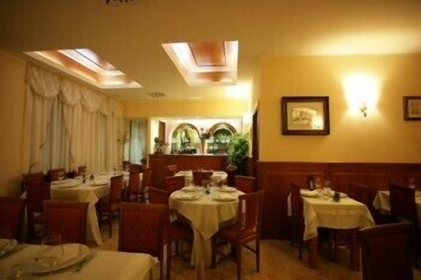 Un restaurante con varias mesas y sillas, una paleta de colores cálidos y una araña.