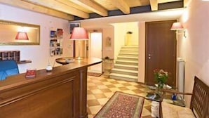 A hotel lobby with a reception desk, a check-in counter, a staircase, and a patterned rug. - Hotel Capitelli (Trieste)