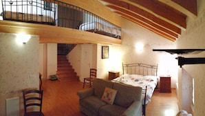 A spacious living area with a high ceiling, wooden beams, a staircase, a sofa, a bed, and a small table. - Hotel Capitelli (Trieste)