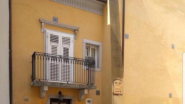 A two-story building with a yellow facade, a wooden door, and a small balcony with a metal railing. - Hotel Capitelli (Trieste)