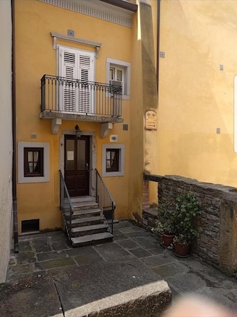 A two-story building with a yellow facade, a wooden door, and a small balcony with a metal railing.
