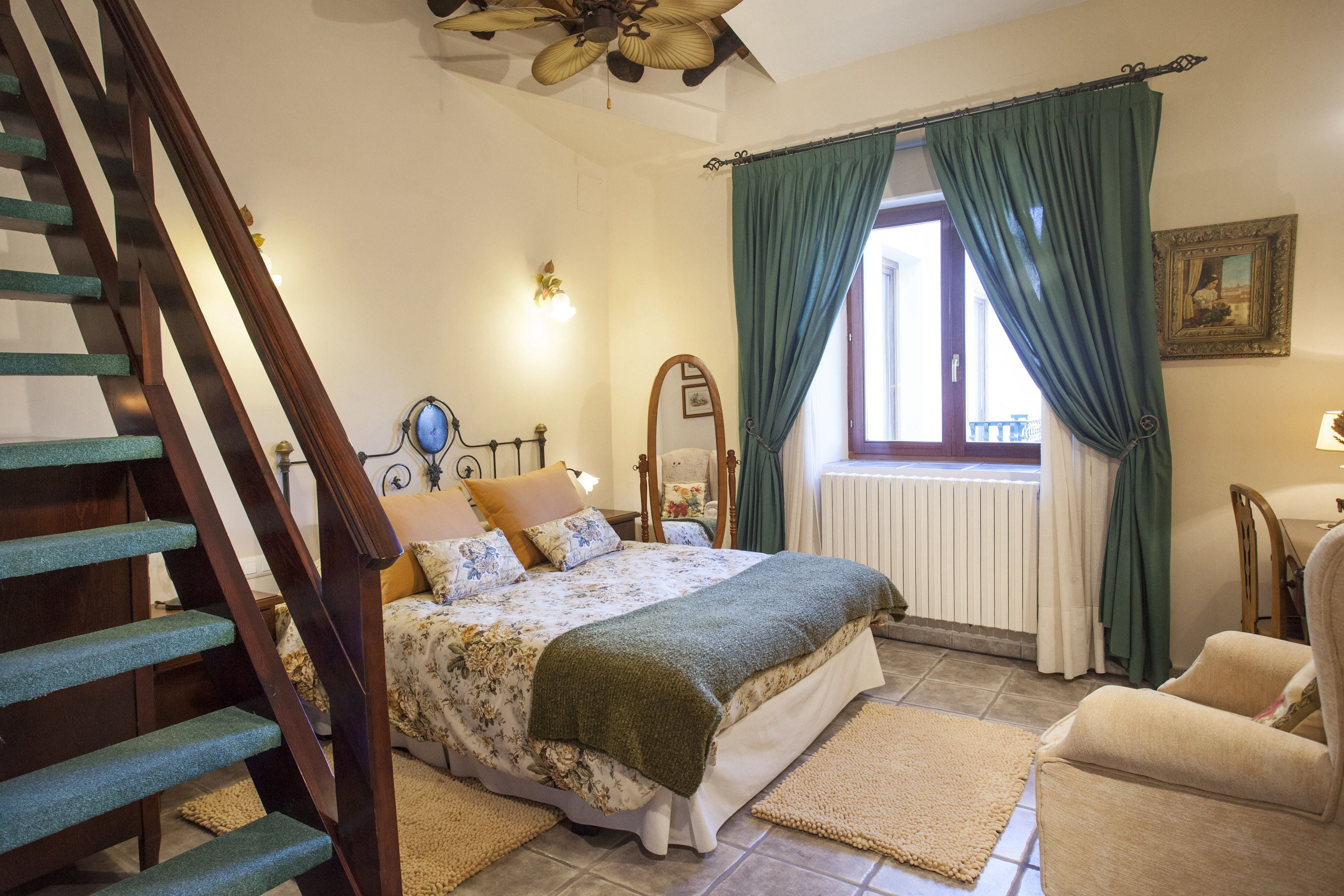 A bedroom with a bed, a chair, a window with curtains, a radiator, and a staircase.
