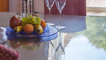 Una mesa de comedor con una bandeja de frutas, dos copas de vino y un mantel individual azul.