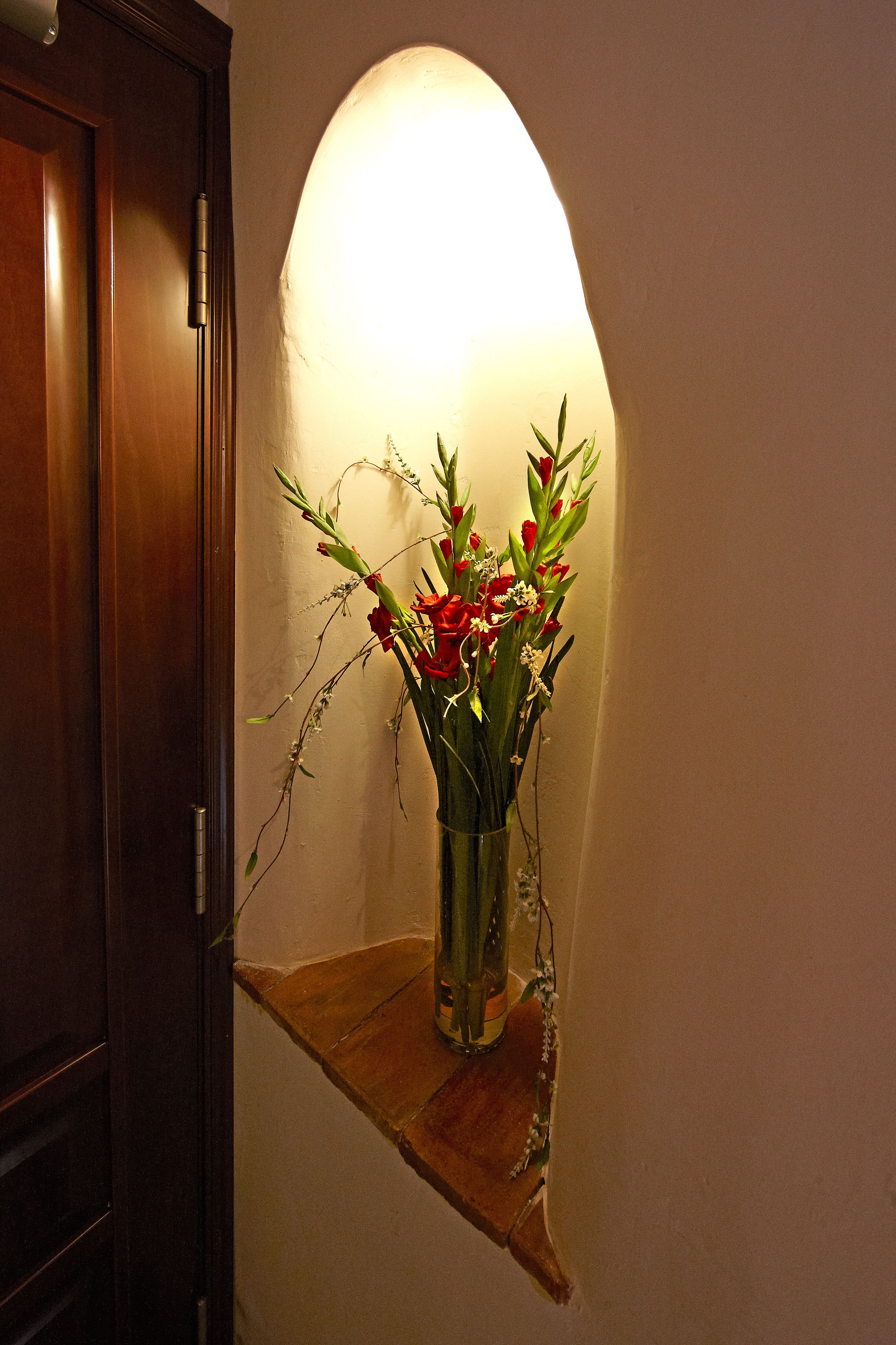 Une porte en bois et une étagère fixée au mur, sur laquelle se trouve un vase de fleurs.