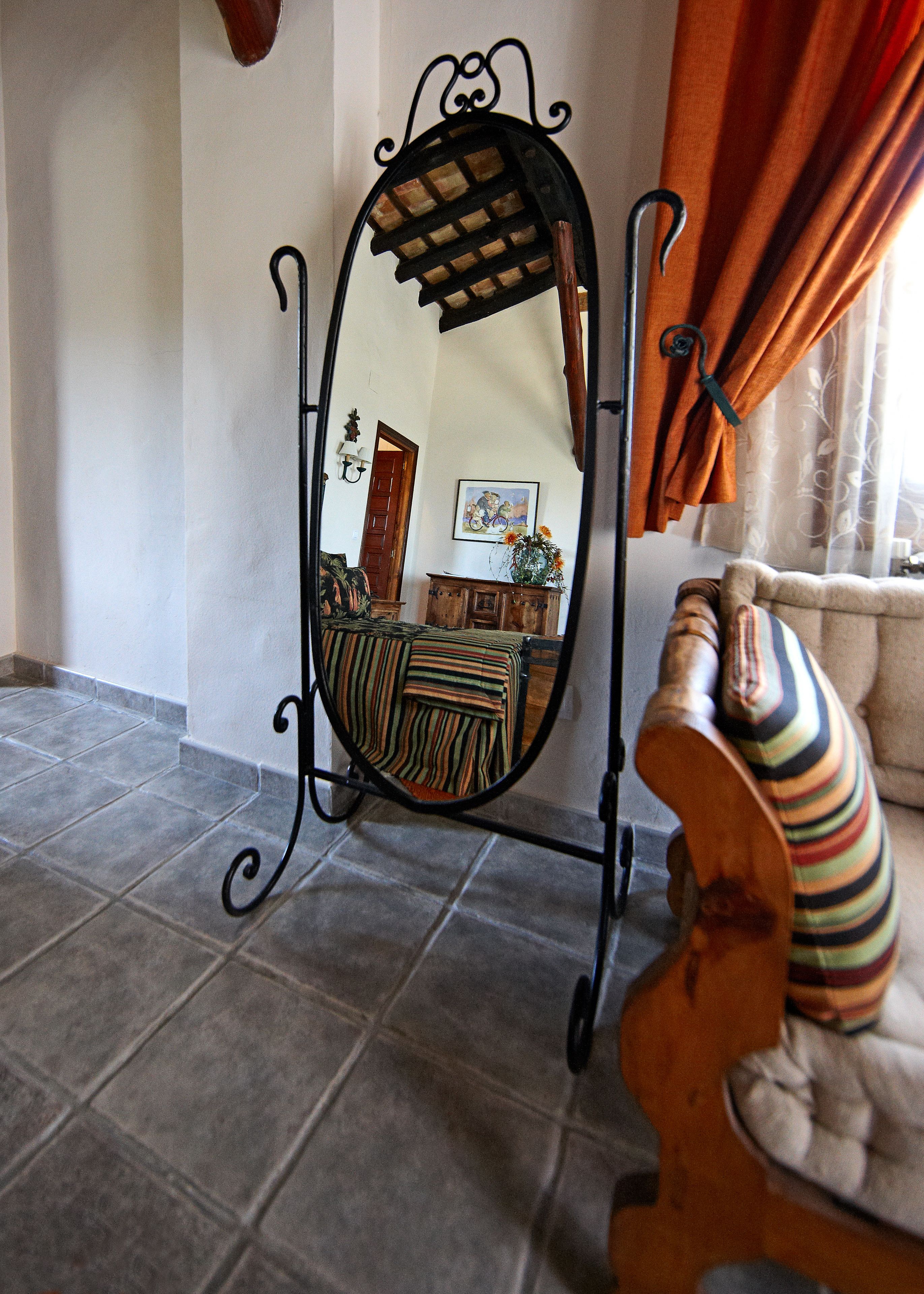 Una habitación con un espejo grande que refleja un comedor, un banco de madera con un cojín a rayas, y una puerta que da a otra habitación.
