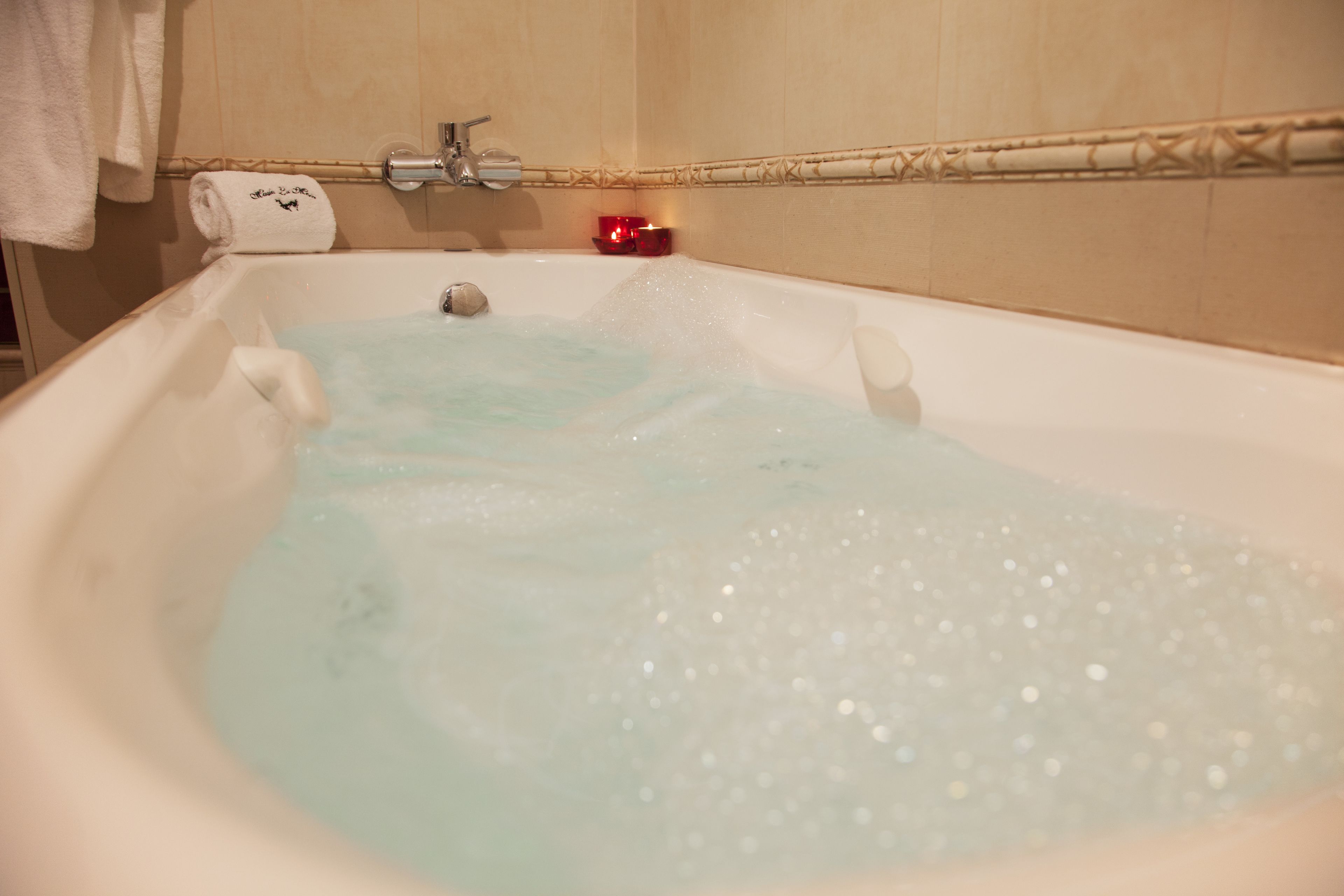 A bathtub filled with water and bubbles, a towel, and a candle on the side.