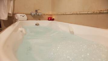A bathtub filled with water and bubbles, a towel, and a candle on the side.