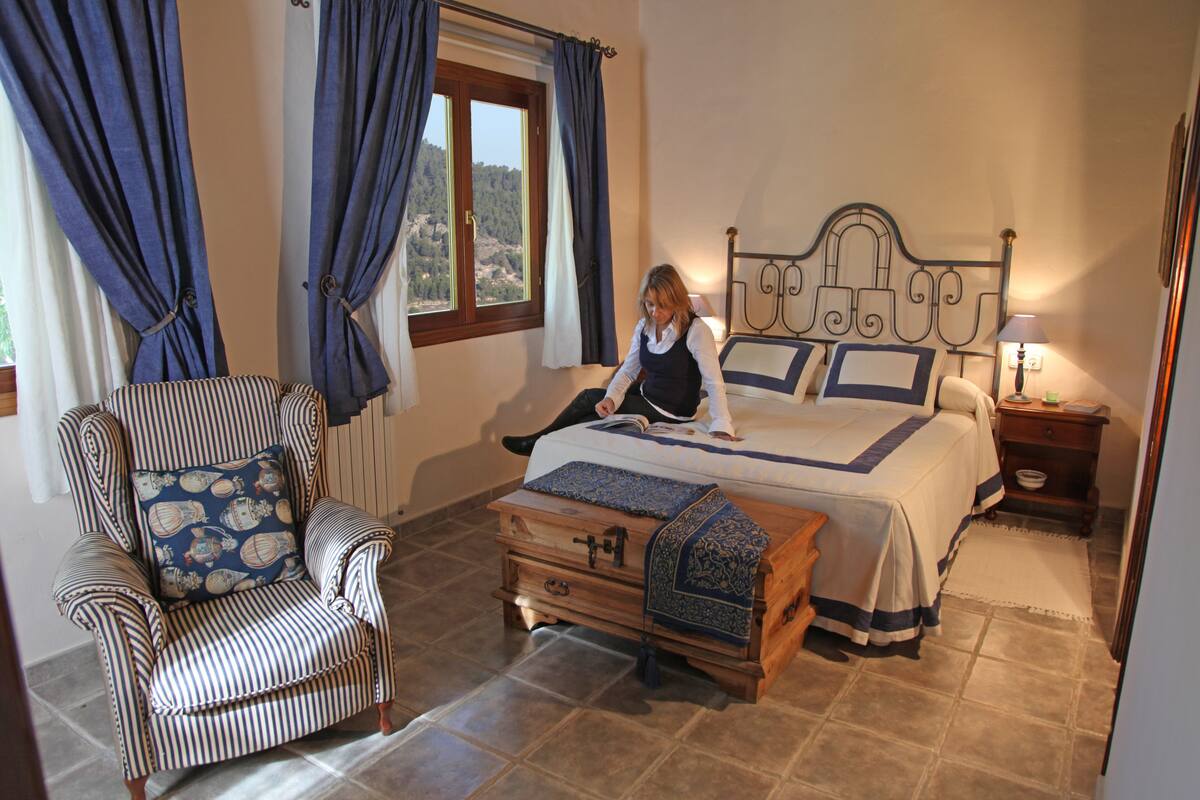 A bedroom with a bed, a chair, a nightstand, and a window with curtains.