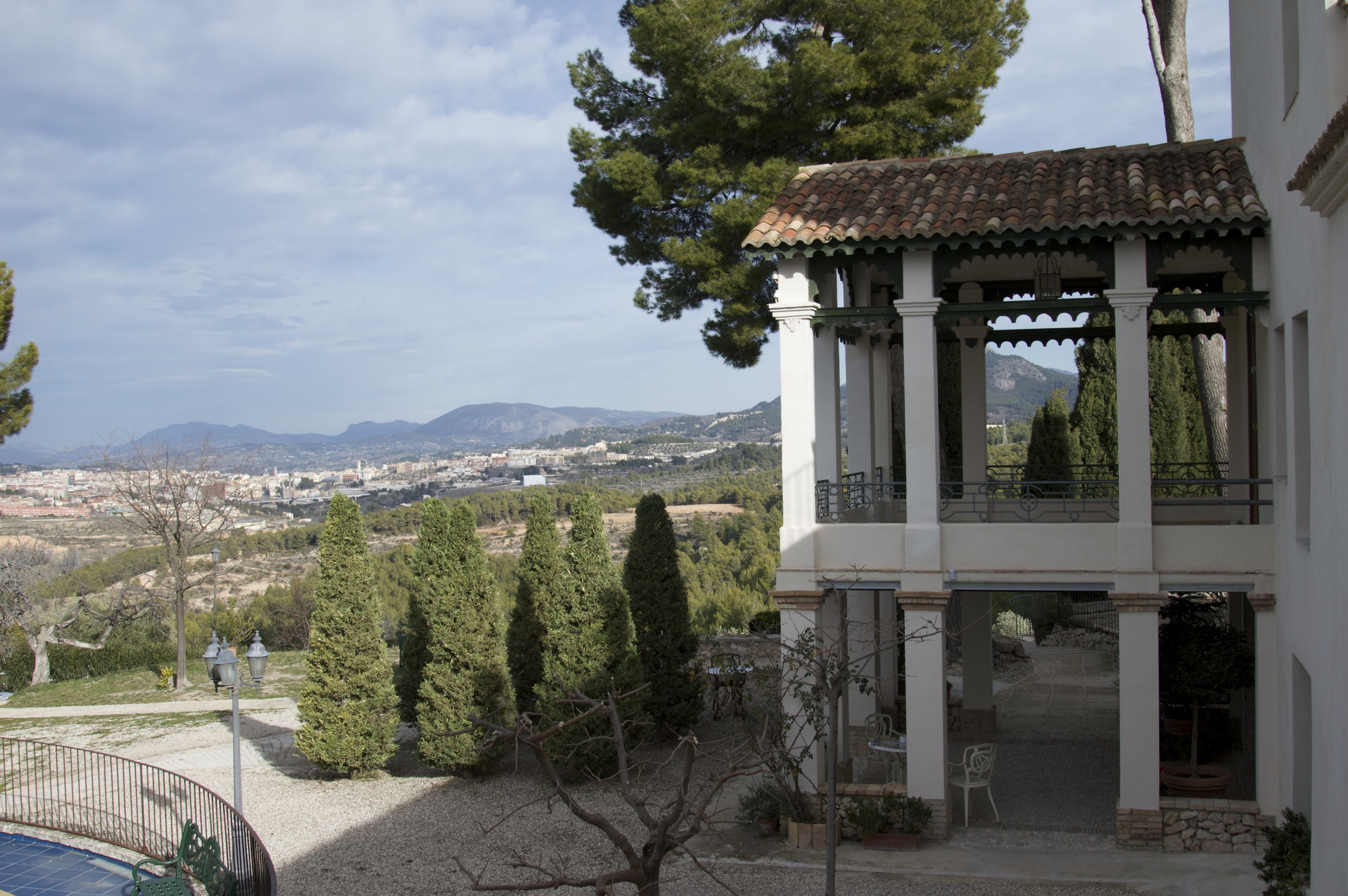 Ein Gebäude mit einem Balkon, der auf eine Stadtlandschaft und Berge blickt.