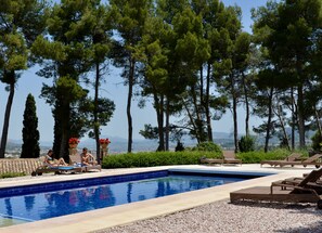 A pool area with lounge chairs, a tiled pool, and tall trees in the background. - Masia La Mota (Alcoy)