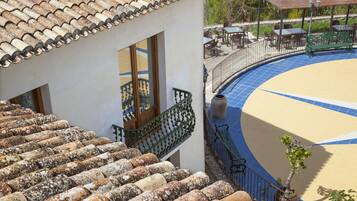 Un edificio con techo de tejas, un balcón con baranda verde y una zona de piscina con borde curvo.