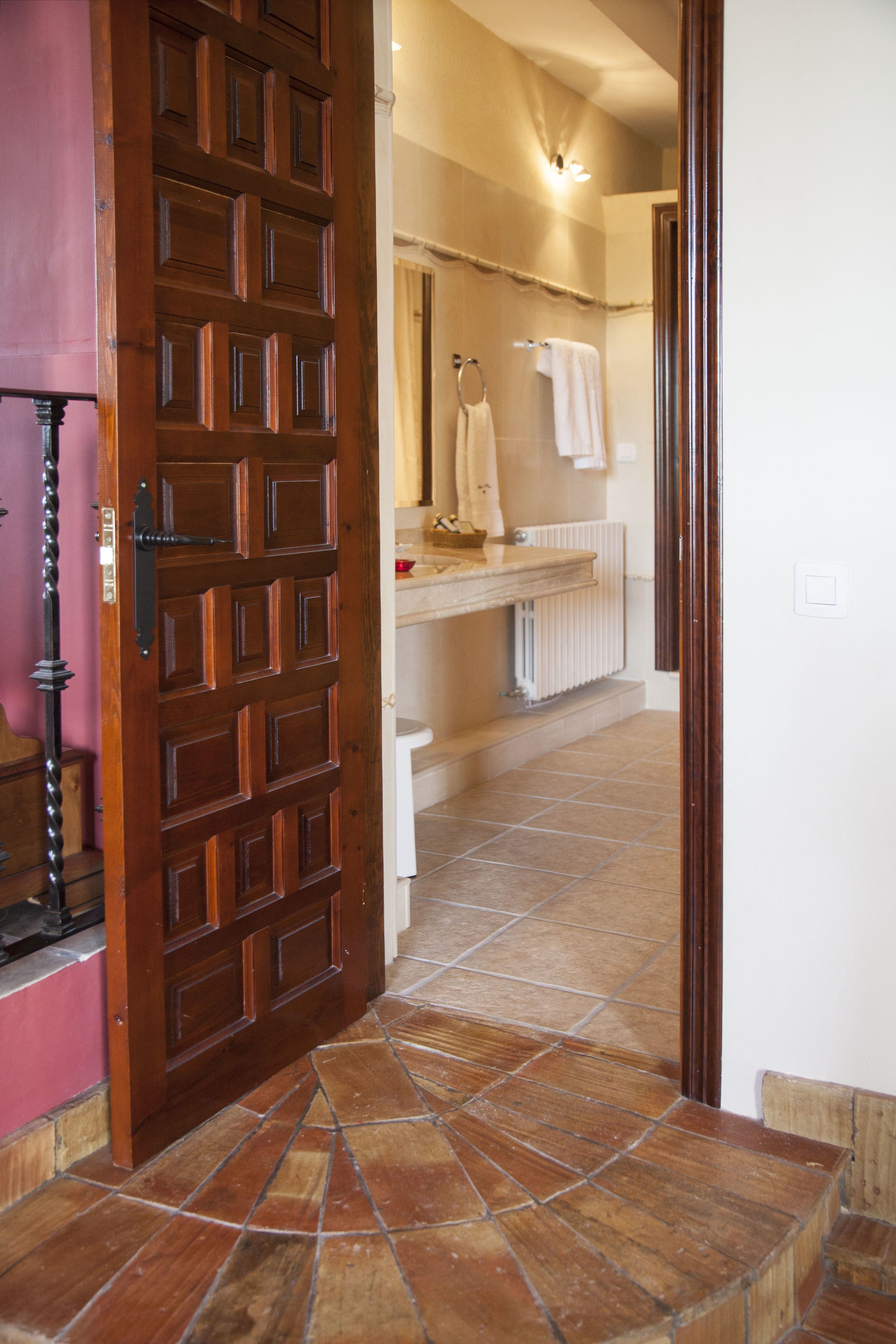 Una puerta de madera que da a un baño con suelo de baldosas y un perchero.