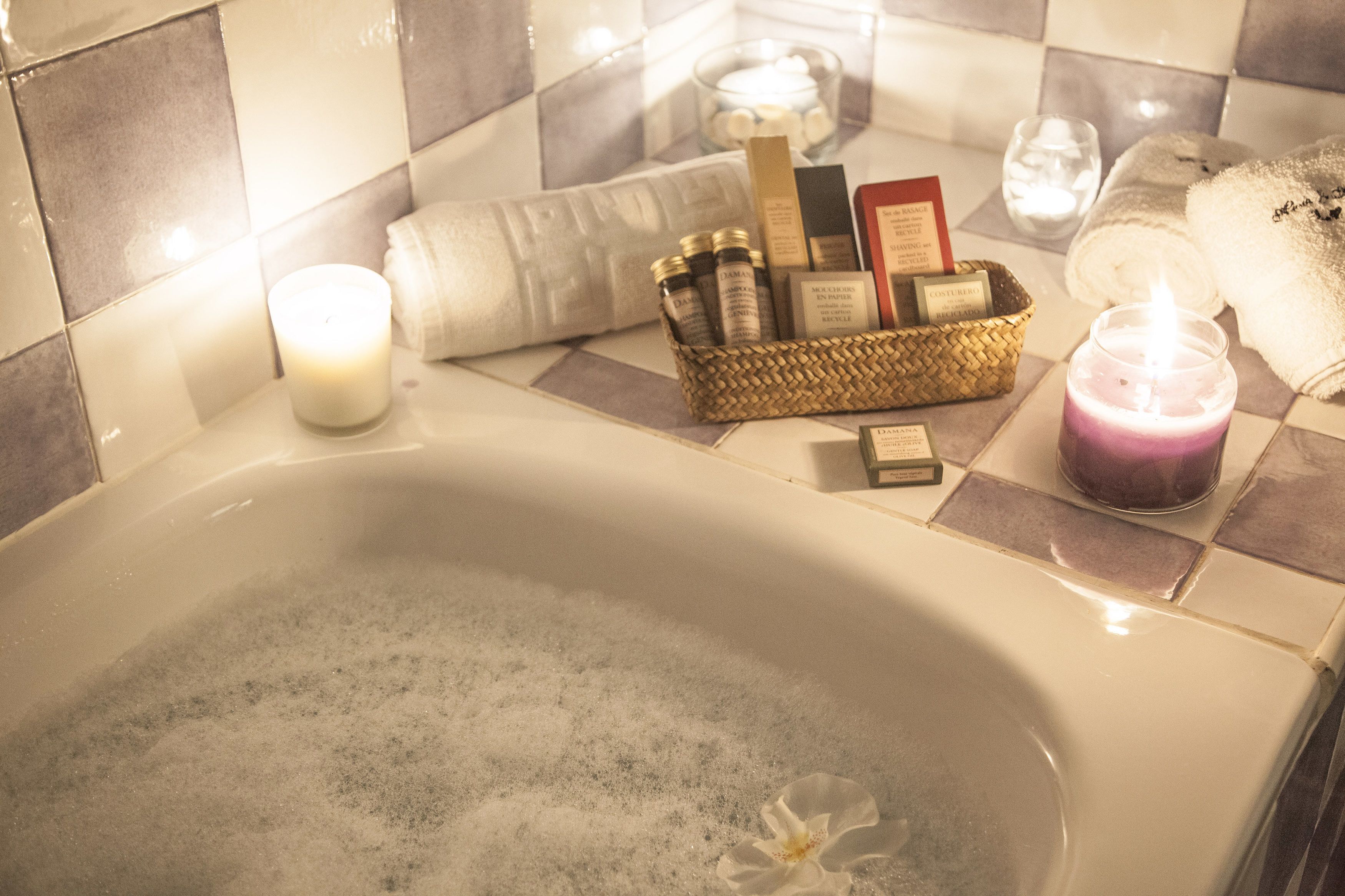 A bathtub with a floral decoration, a candle, and a basket of toiletries.