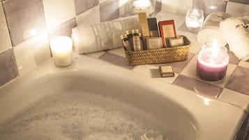 Una bañera con decoración floral, una vela y una cesta de artículos de tocador.