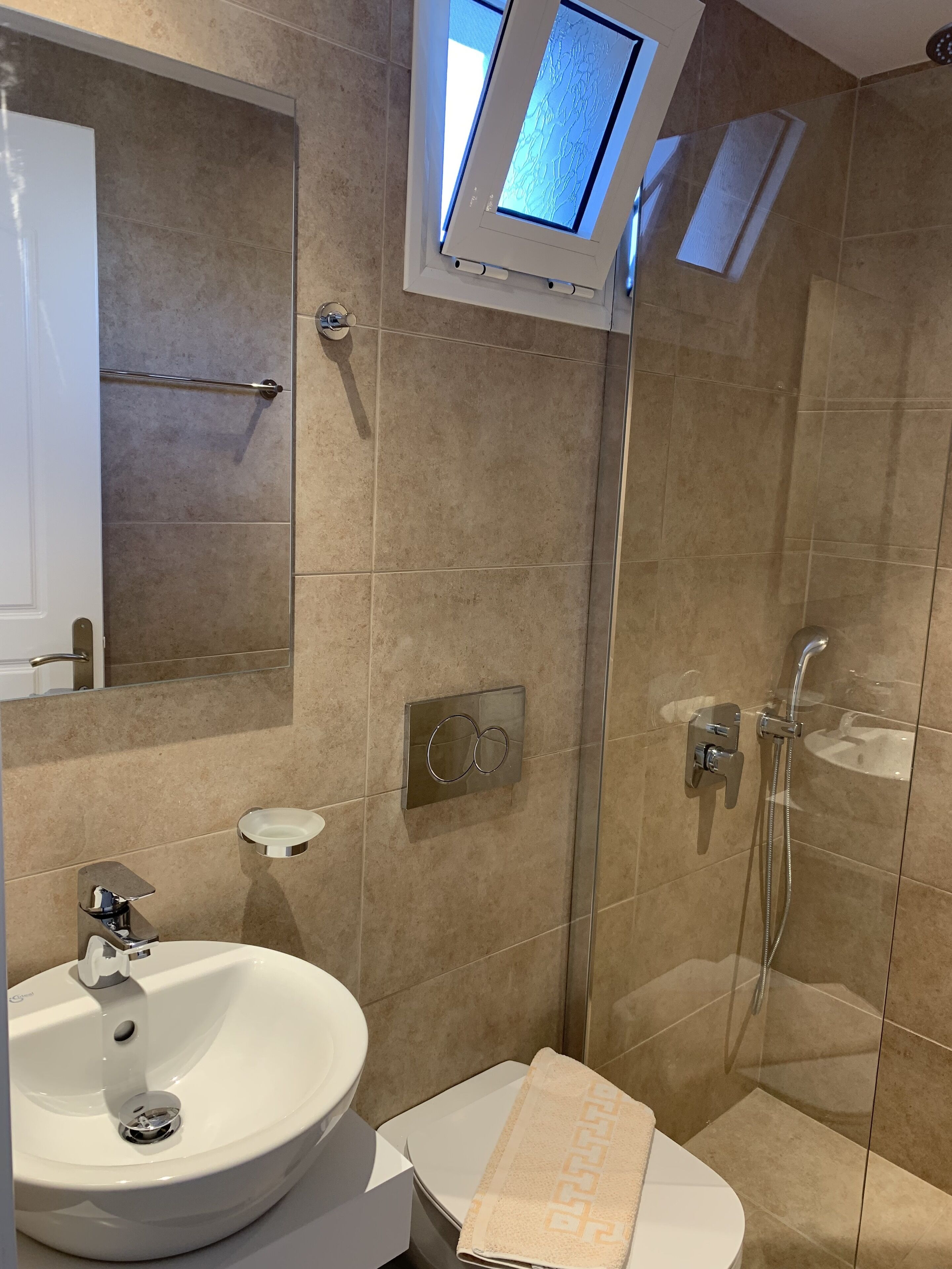 Un baño moderno con lavamanos blanco, cabina de ducha de vidrio y un perchero para toallas.