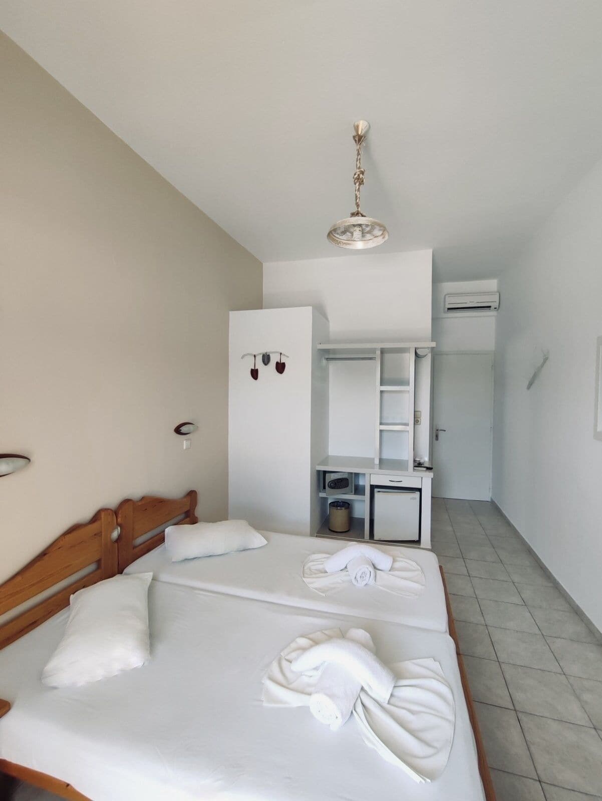 A hotel room with a bed, a desk, a mirror, and an air conditioning unit.