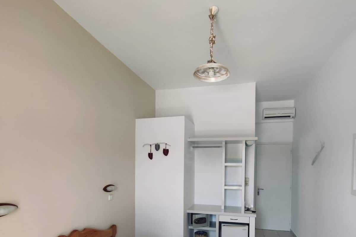 A hotel room with a bed, a desk, a mirror, and an air conditioning unit.
