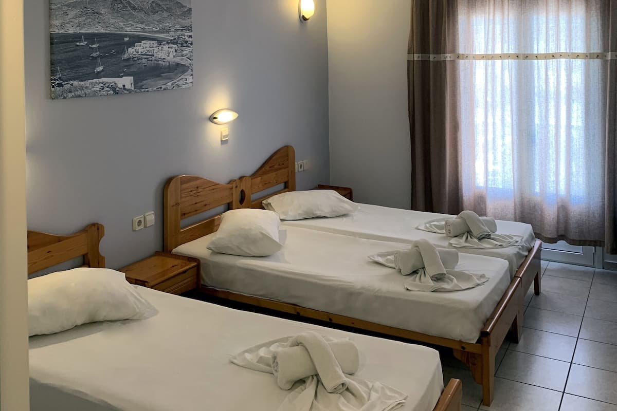 A hotel room with three wooden beds, a painting on the wall, and a window with curtains.