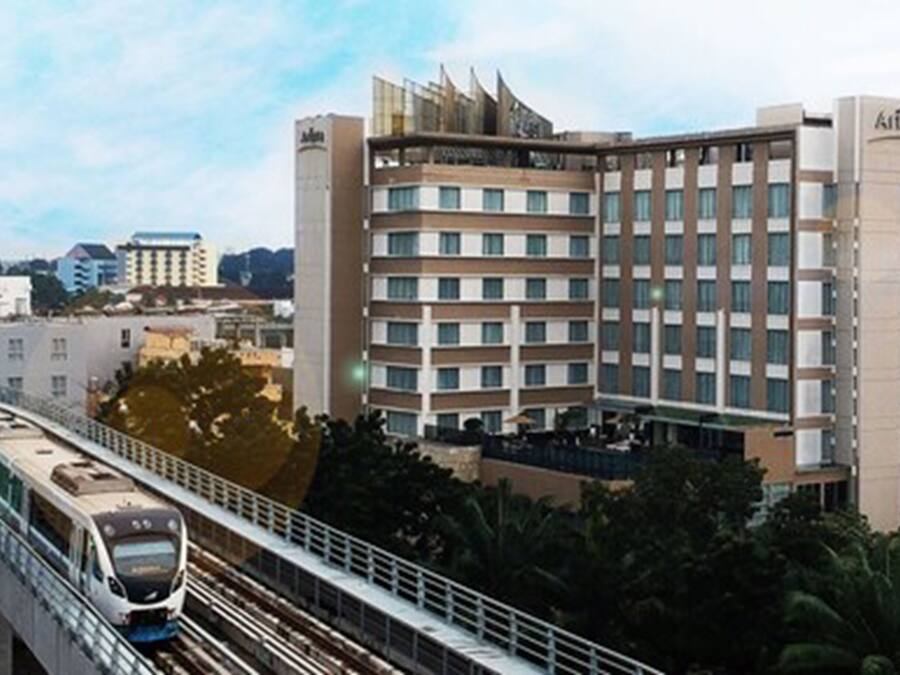 A modern hotel with multiple floors, a train passing by, and a bridge in the foreground.