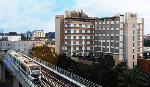 A modern hotel with multiple floors, a train passing by, and a bridge in the foreground.