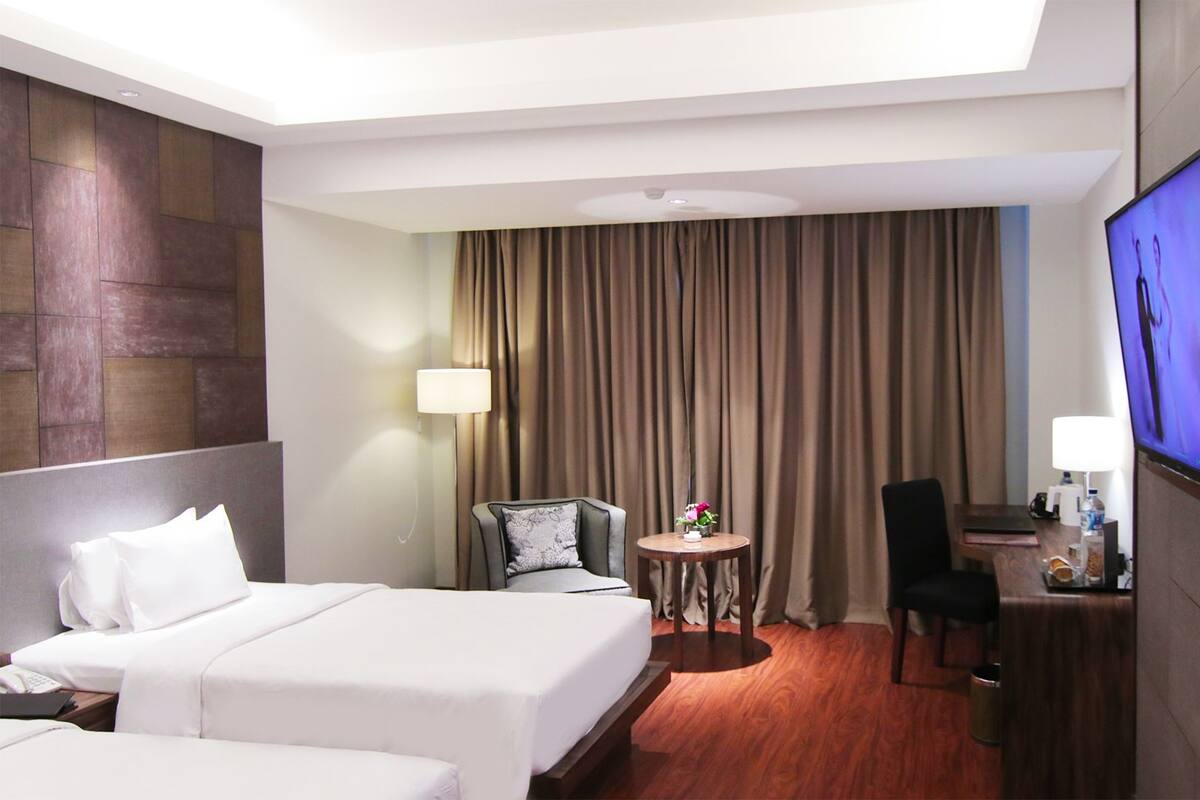 A hotel room with two beds, a desk with a chair, a TV, and a small table with a lamp.