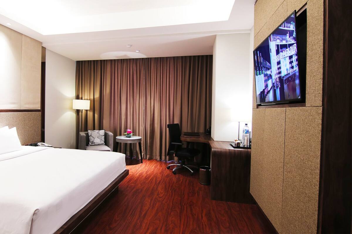 A hotel room with a large bed, a desk, a chair, a television, and a window with curtains.