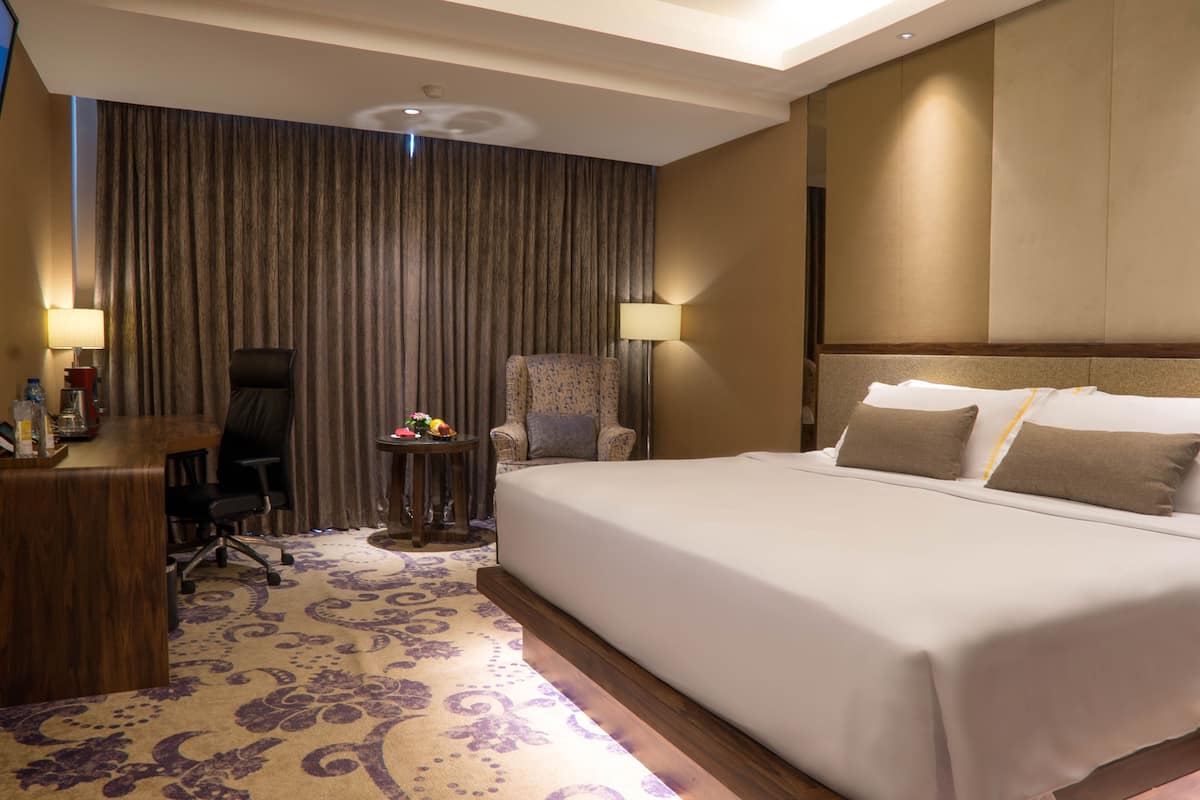 A hotel room with a large bed, a desk, a chair, a small table with flowers, and a curtain.