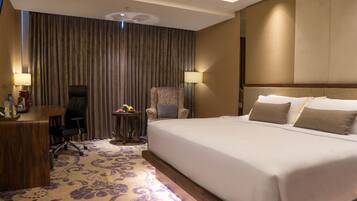 A hotel room with a large bed, a desk, a chair, a small table with flowers, and a curtain.