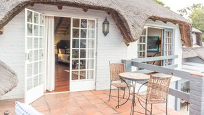 Una cabaña con techo de paja y un patio con sillas de mimbre y una mesa.