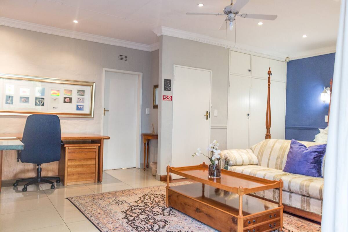 A living room with a sofa, a coffee table, a desk with a chair, and a ceiling fan.
