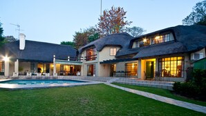 Una casa de dos pisos con piscina, mobiliario de exterior y un césped bien cuidado.