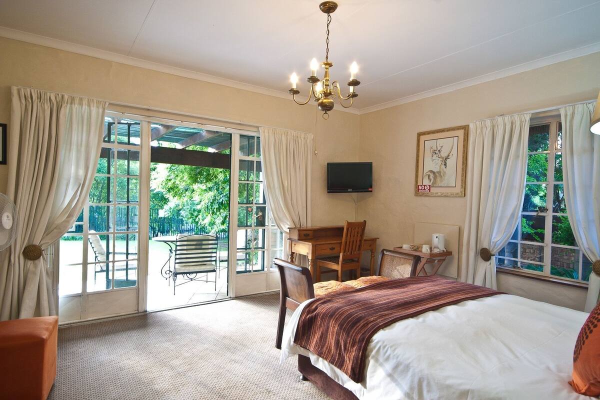 A bedroom with a bed, a desk, a chair, a television, and a view of the outdoors.