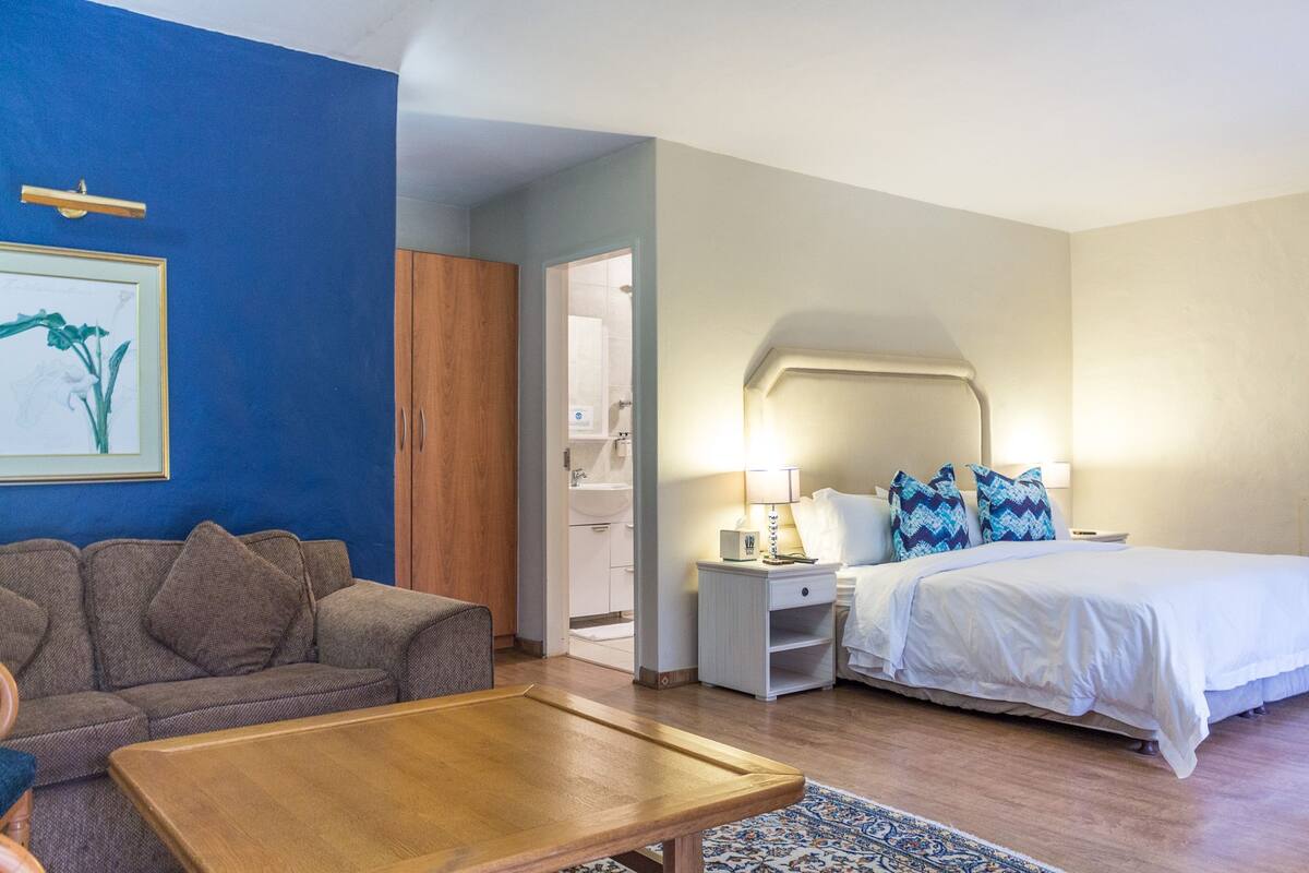 A hotel room with a bed, a nightstand, a sofa, a coffee table, and a bathroom visible through an open door.