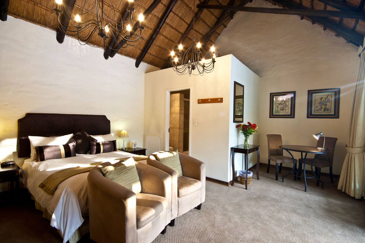 A hotel room with a large bed, a sofa, a dining table with chairs, and a chandelier.