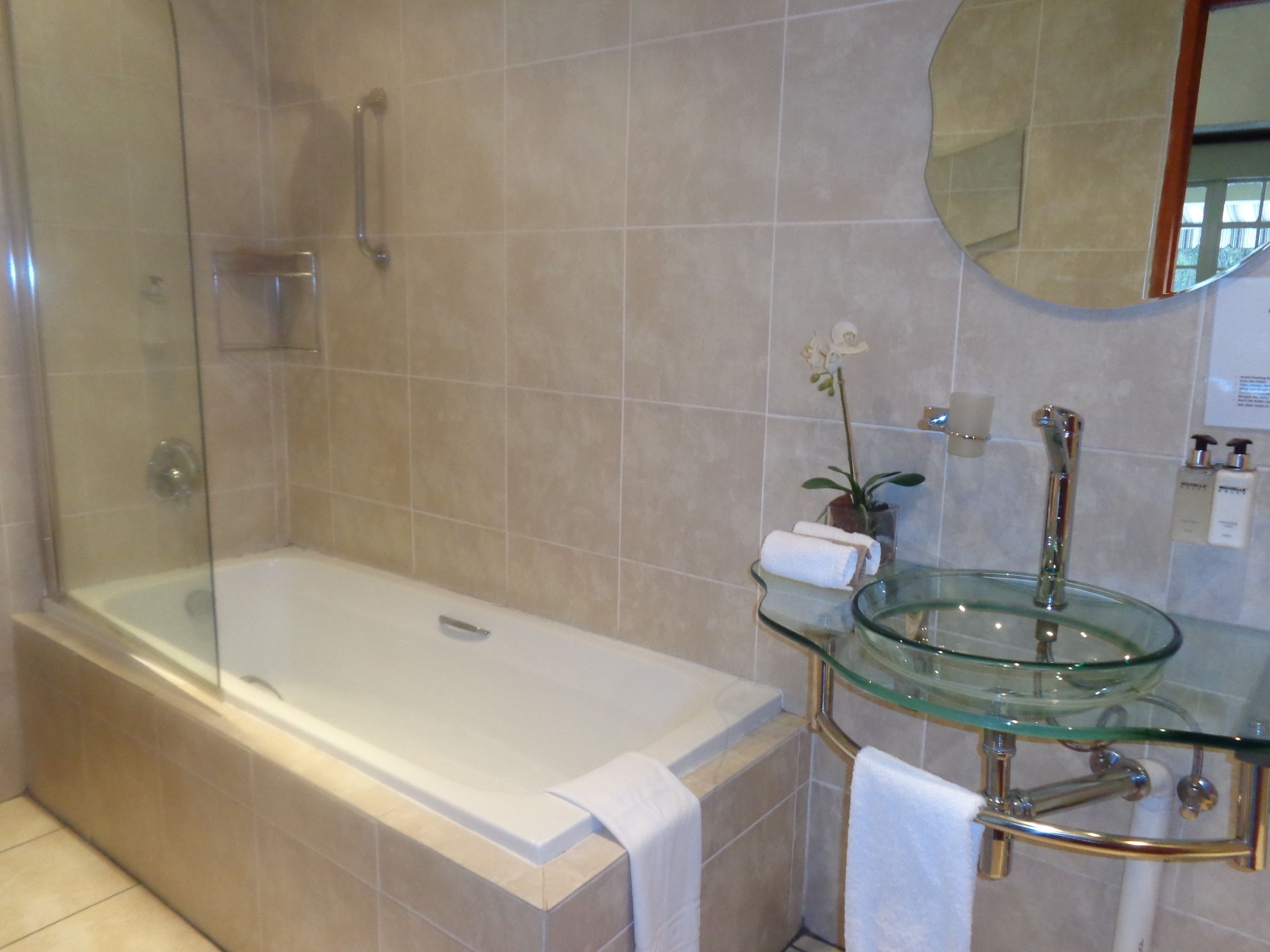A modern bathroom with a glass-enclosed shower, a glass sink, and a large mirror.