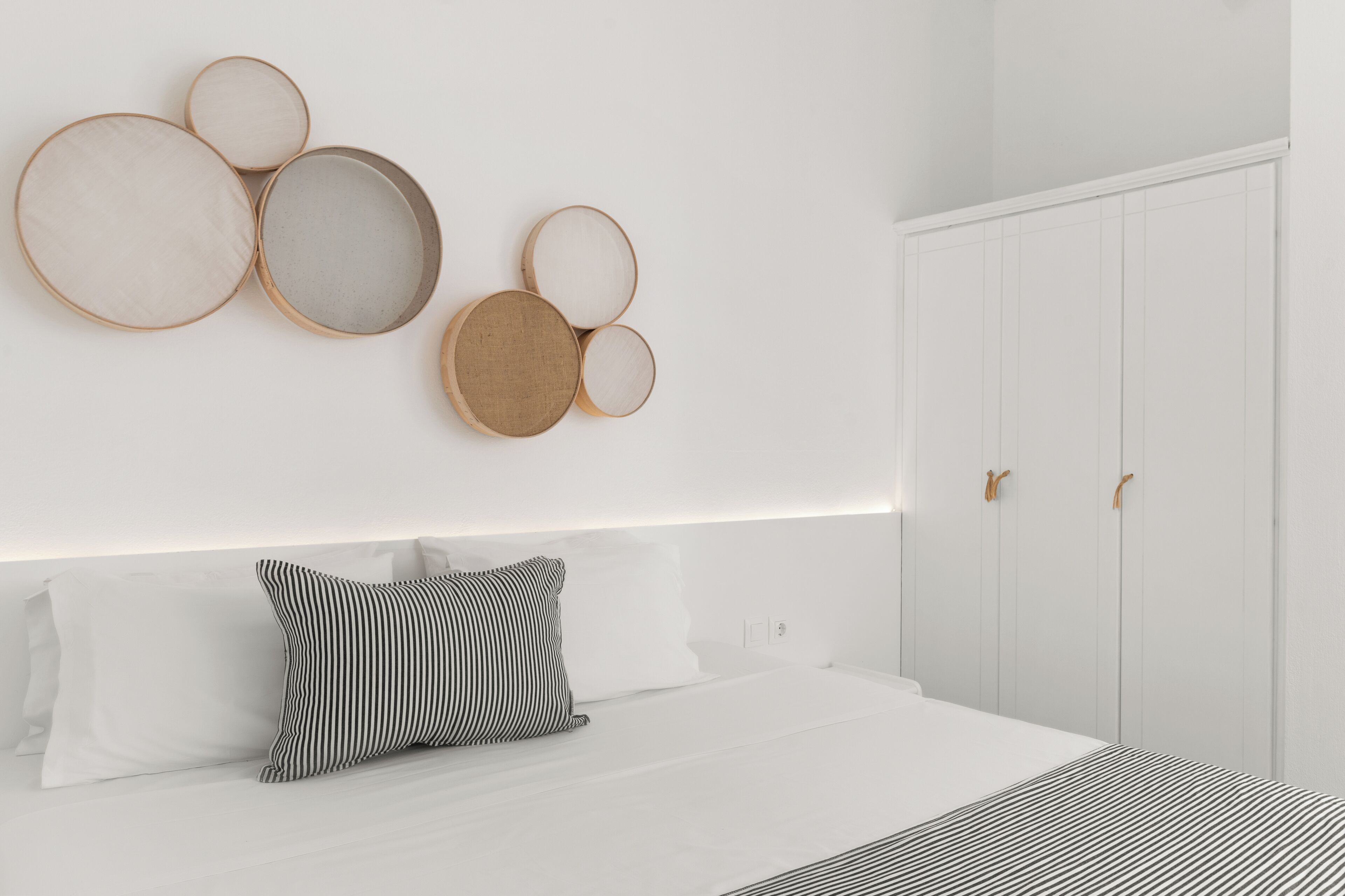 A modern bedroom with a large bed, a headboard, a wardrobe, and wall-mounted circular mirrors.