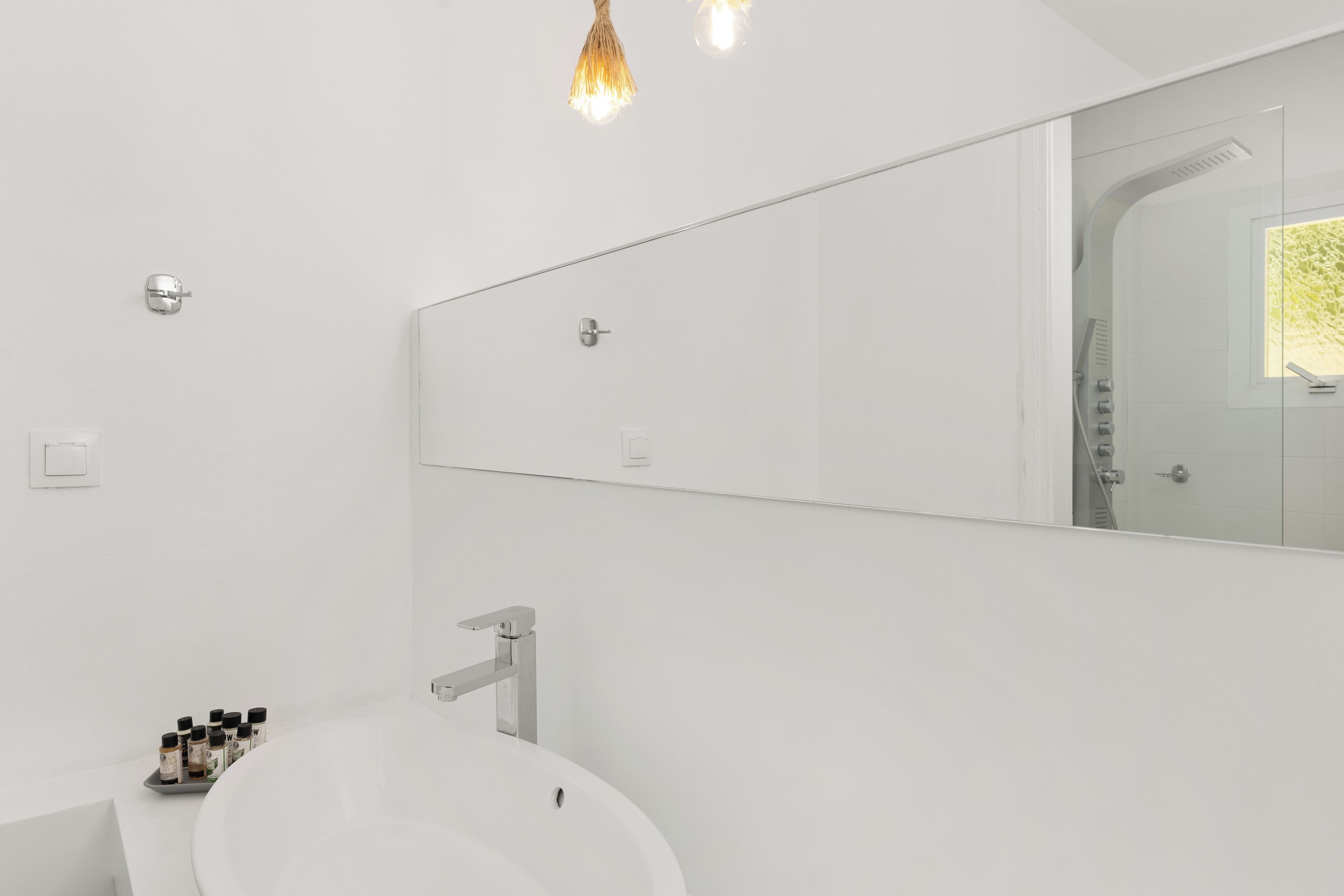 Un baño moderno con un espejo grande, un lavamanos blanco y una lámpara sobre el espejo.