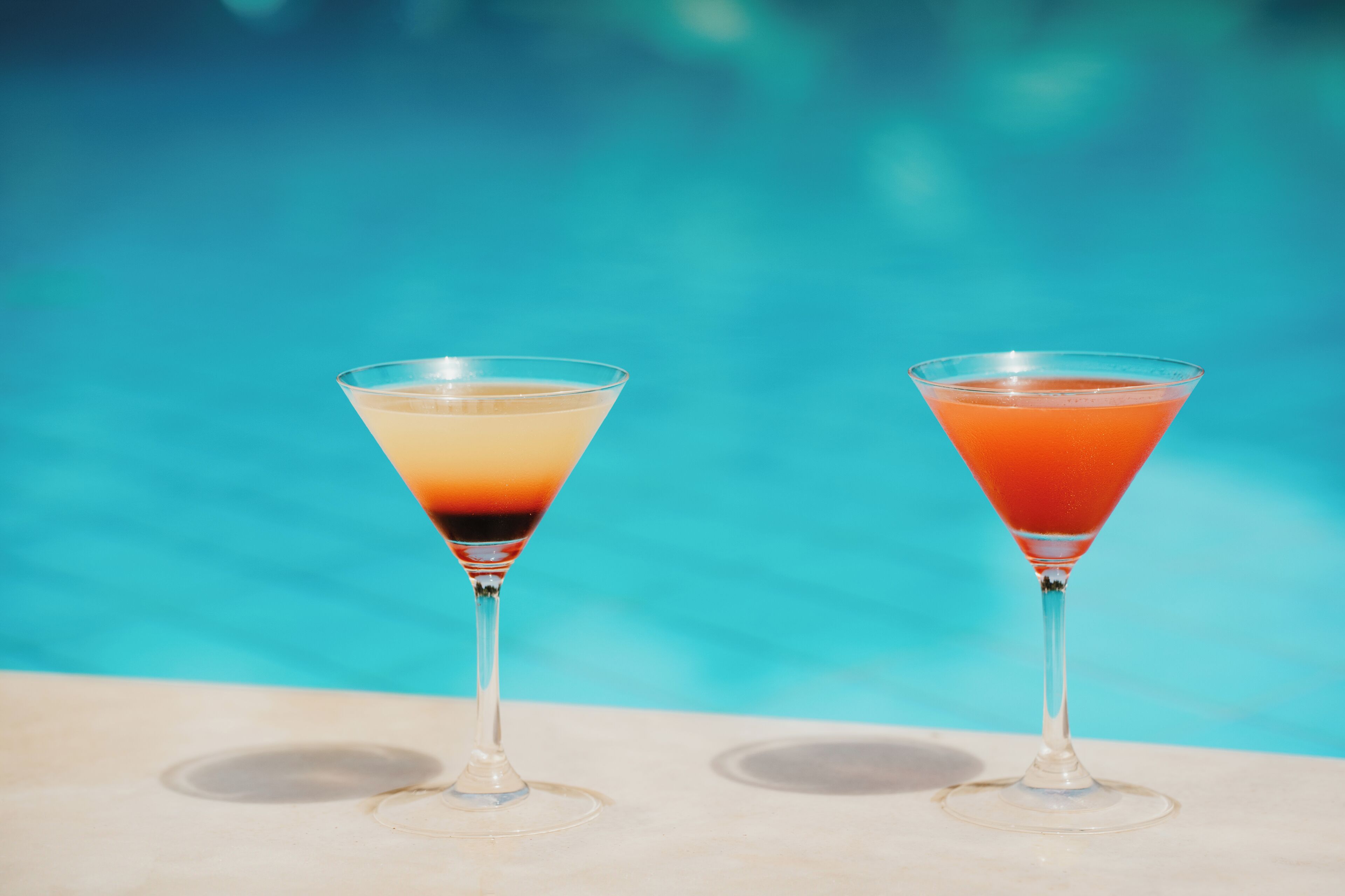Two martini glasses with layered drinks by a pool.
