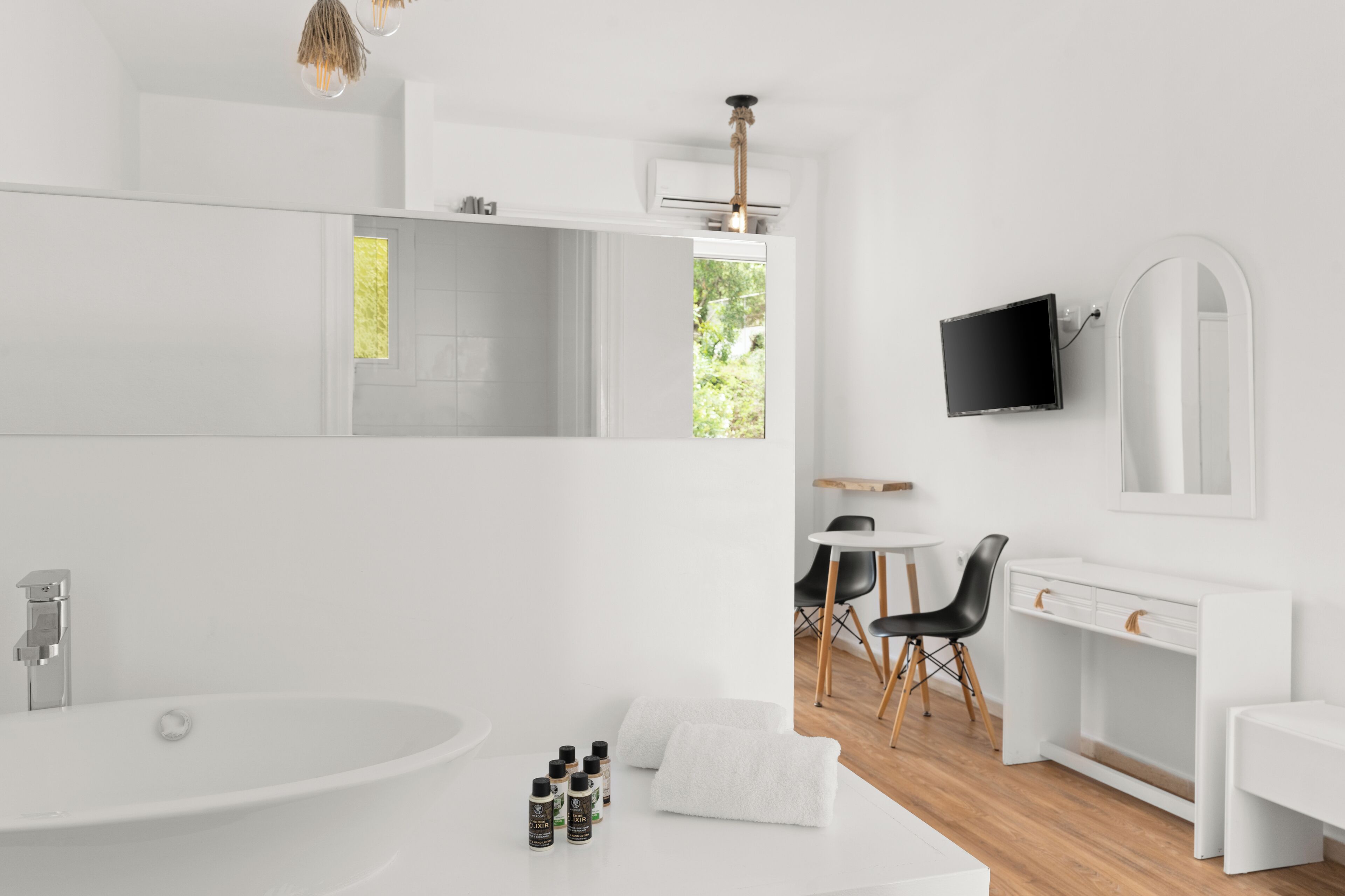 Un baño moderno con una bañera blanca grande, un tocador con espejo y un televisor de pantalla plana montado en la pared.