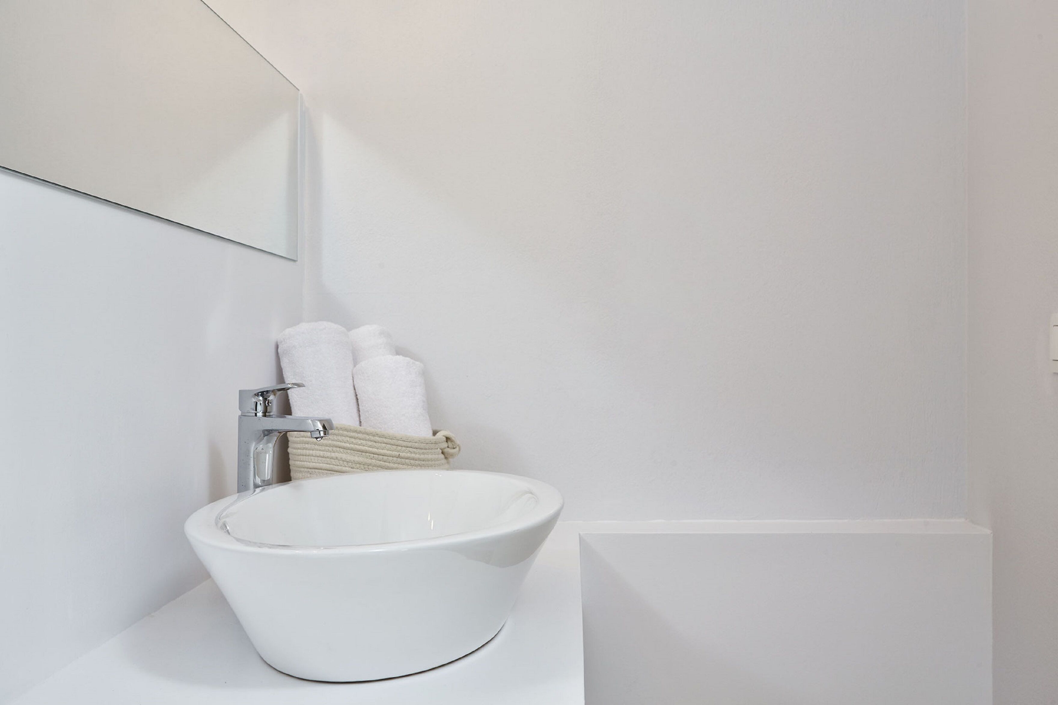 A white bathroom with a large mirror, a white sink, and two white towels hanging on the wall.