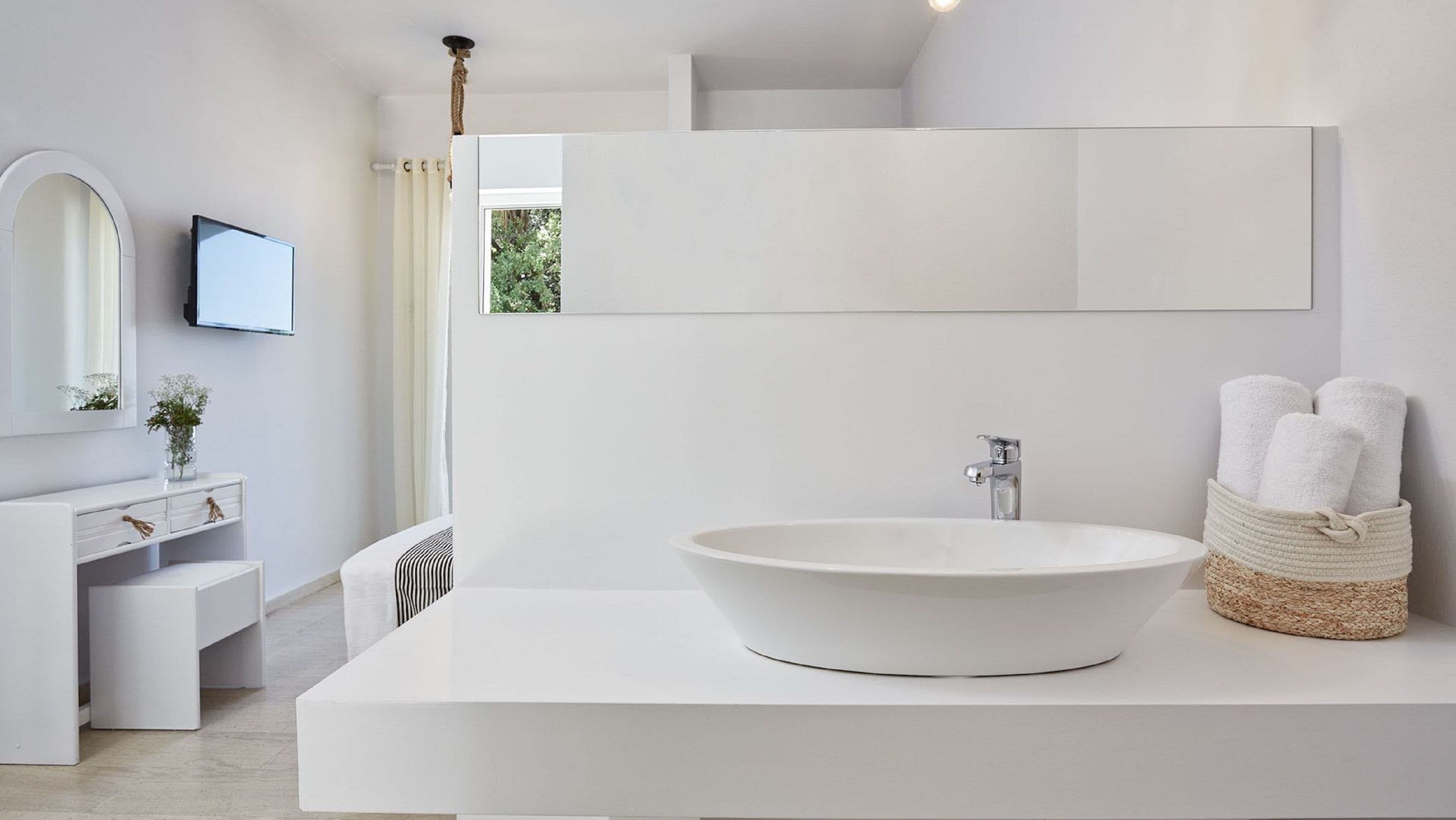 A modern bathroom with a large white sink, a mirror, and a TV mounted on the wall.