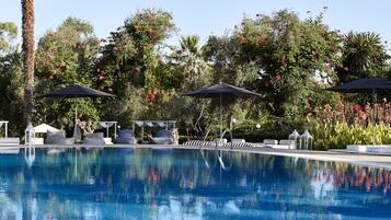 A clear blue pool with lounge chairs and umbrellas, surrounded by lush greenery and trees.