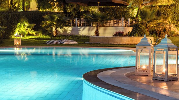 A swimming pool with two white lanterns on the edge, surrounded by greenery and a gazebo in the background. - Mr and Mrs White Corfu Couples Retreat Adults Only (Corfu)